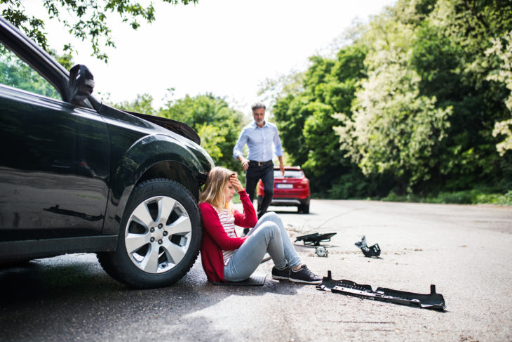Chica sentada en el piso después de haber tenido un accidente automovilístico