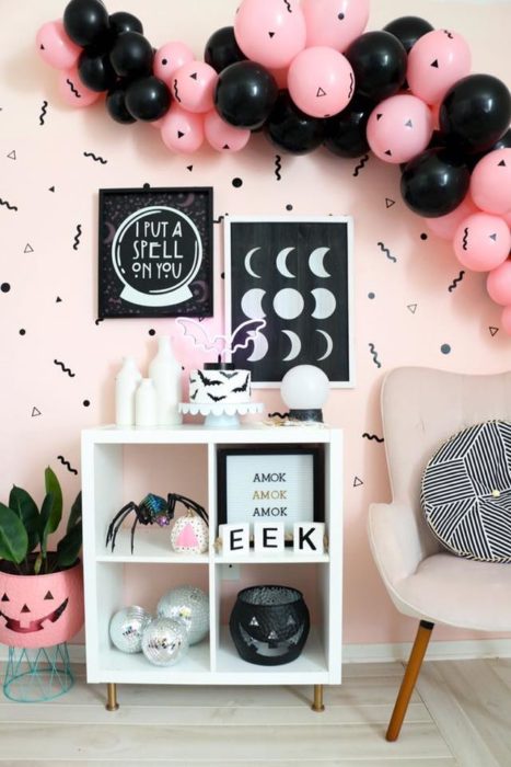 Habitación con pared rosa y detalles negros con muebles blancos y globos rosas y negros para Halloween