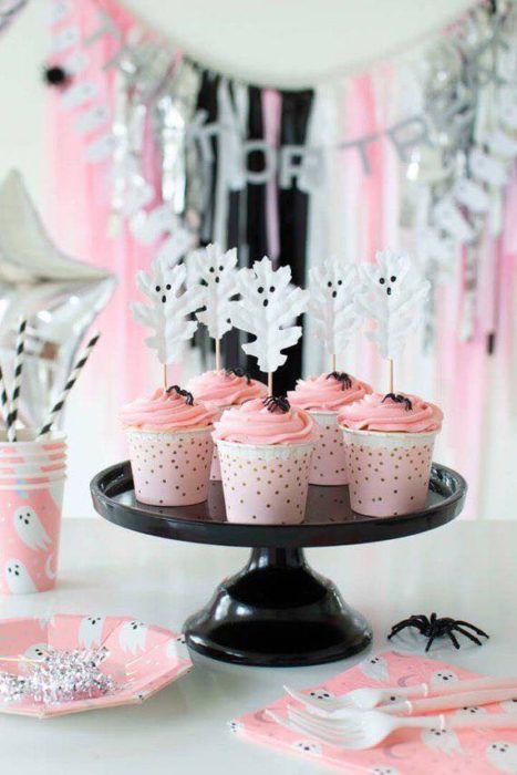Cupcakes rosas decorados con fantasmas en un palillo, presentados en base negra