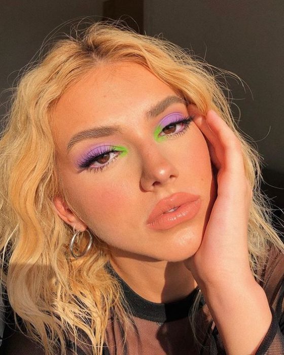 Chica rubia de cabello rizado con maquillaje de ojos morado y un toque de verde, labios nude
