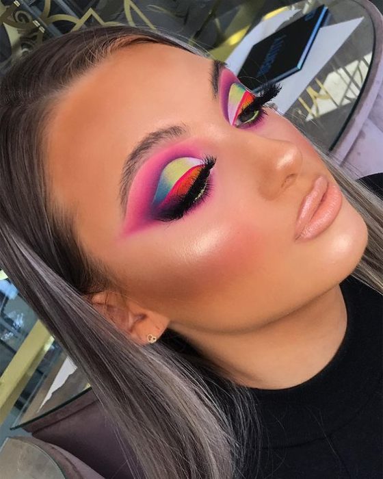 Chica rubia con maquillaje colorido rosa y detalles azules y verdes, labio nude