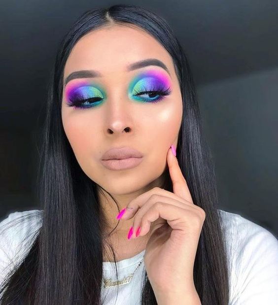 Chica morena de cabello negro suelto con maquillaje en tonos morado, rosa y azul, labio nude