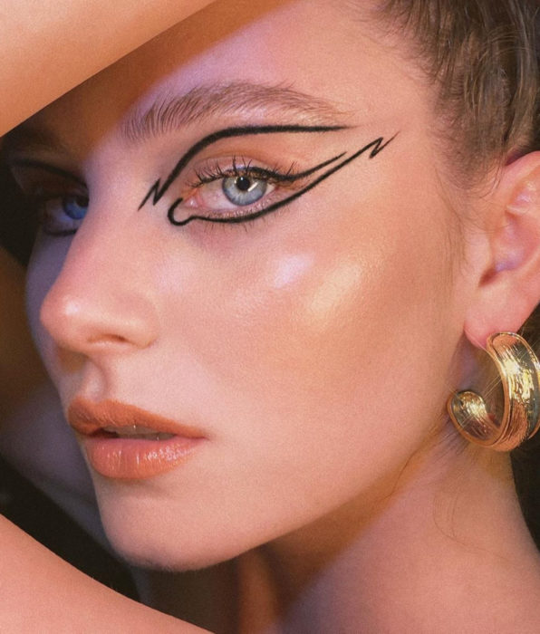 Mujer de ojos azules grises, delineado gráfico color negro, labios rosa durazno