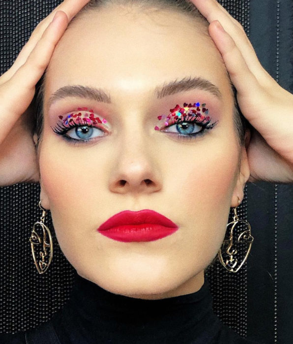Mujer de ojos azules con maquillaje femenino natural, sombra glitter brillos, labial rojo húmedo