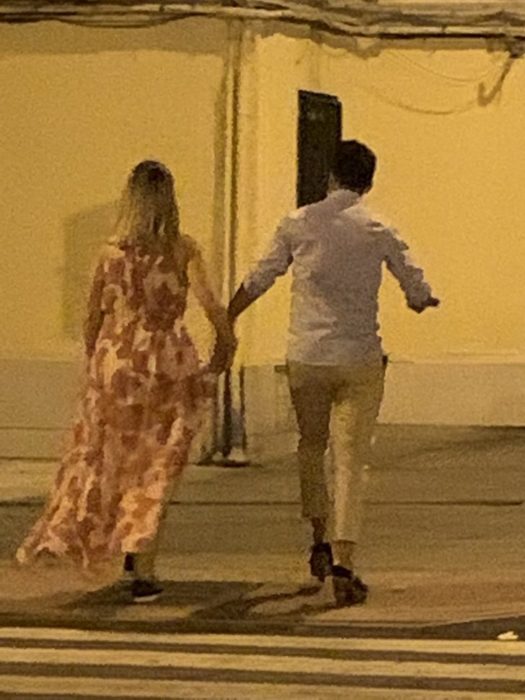 Chico y chica caminando por la calle mientras él usa los tacones de ella