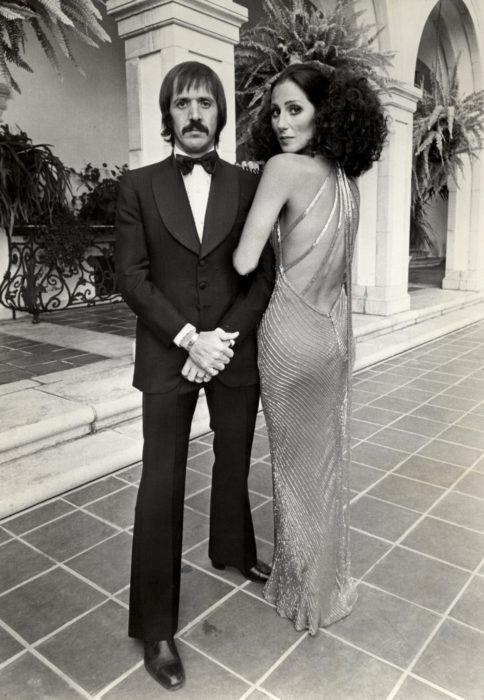 Looks icónicos de Cher; Sonny con traje negro, cabello rizado, vestido de gala