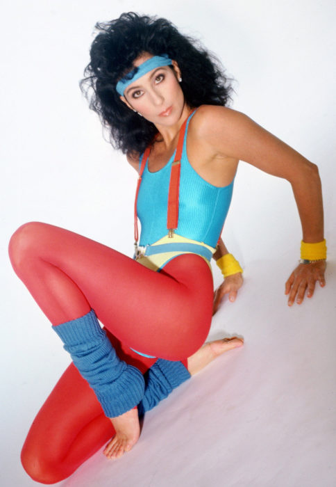 Looks icónicos de Cher; atuendo retro para hacer ejercicio, legging rojo, calentadores azules, cabello negro, esponjado y rizado