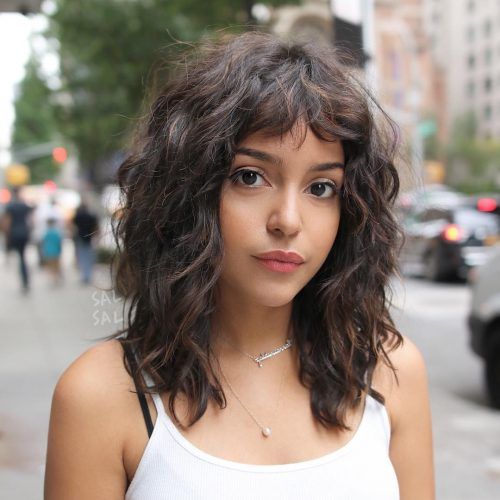 Chica morena con cabello rizado y melena al hombro con blusa blanca de tirantes