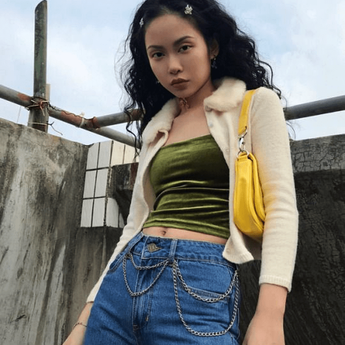 chica de cabello largo oscuro usando una chaqueta teddy blanca con top de terciopelo verde y jeans high-waist a la cintura, bolso amarillo de mano