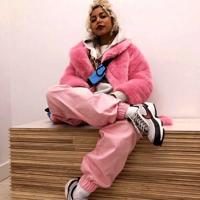chica morena con cabello platinado usando un abrigo teddy rosa con pantalones deportivos rosas y tenis blancos con negro