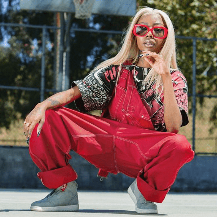 chica morena con cabello rubio usando lentes de sol rojos, overall rojo, camiseta estampada y tenis grises