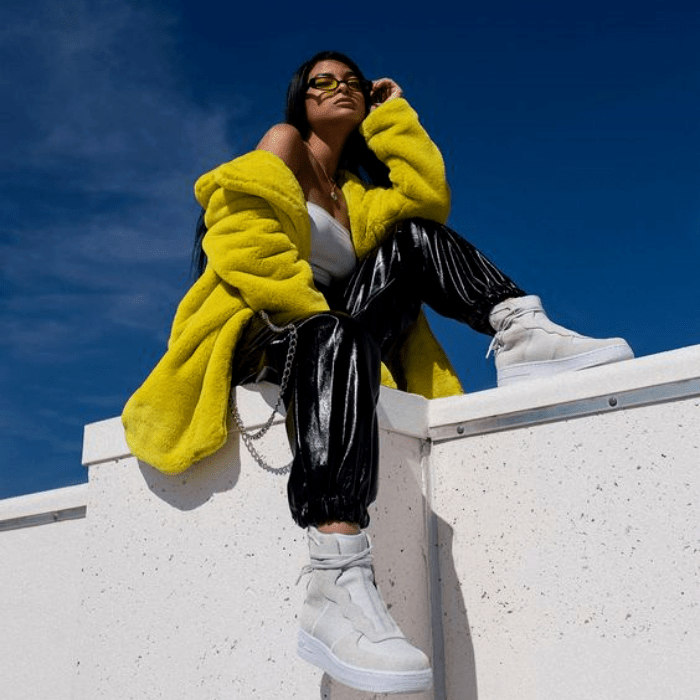 chica morena usando un top blanco, abrigo teddy amarillo, pantalones baggy de cuero y tenis blancos deportivos y lentes de sol
