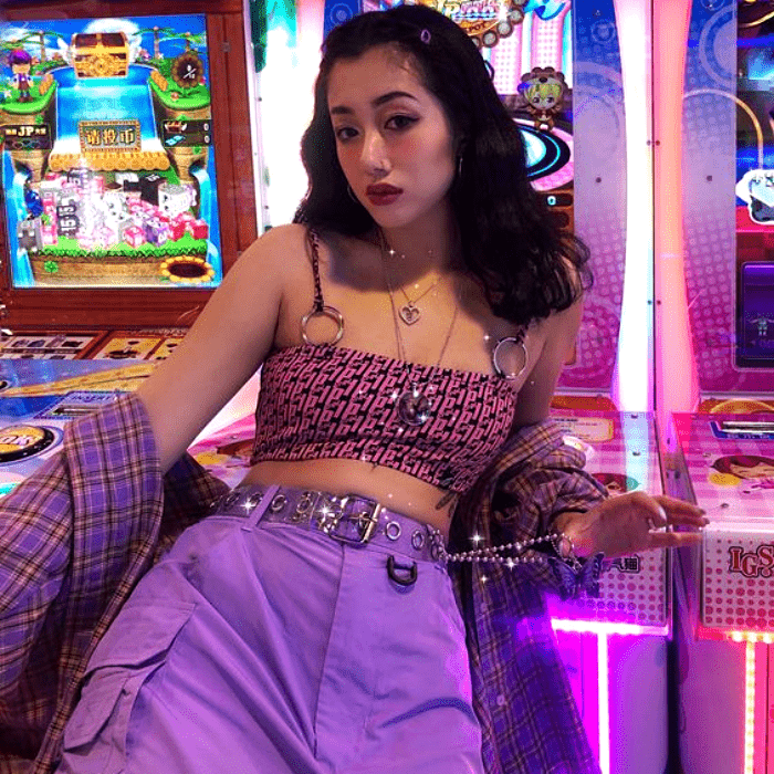 chica de cabello castaño largo usando top de tirantes rosa de cuadros con chaqueta morada y pantalones a la cintura morados con cinturón de cadena
