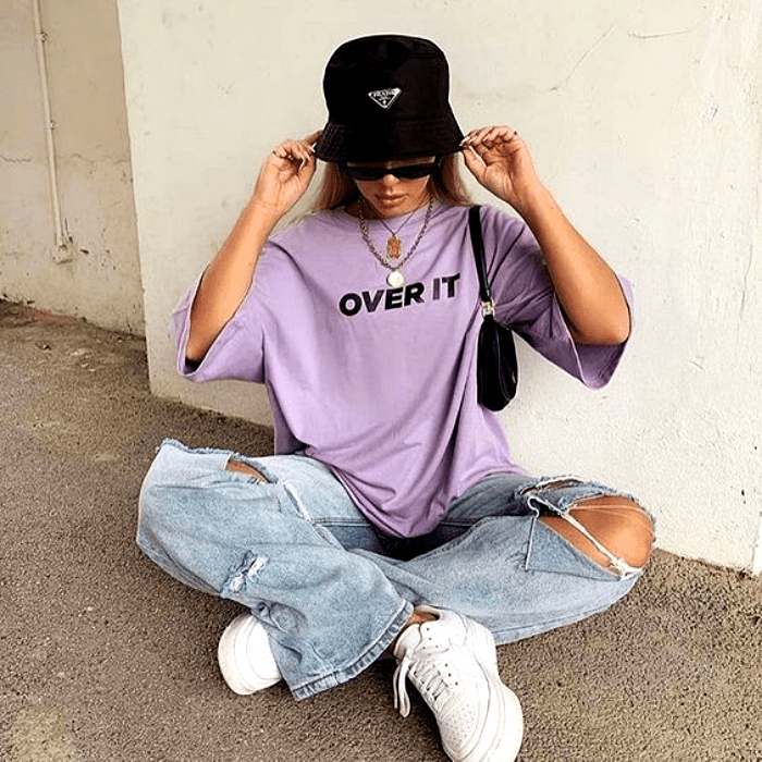 chica rubia usado un bucket-hat negro, camiseta lila, pantalones baggy rotos de las rodillas y tenis blancos