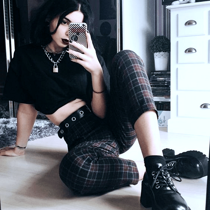 chica de cabello negro usando camiseta crop-top negra, cinturón de estoperoles, pantalón de cuadros negros y guindas con botas de cuero de plataforma