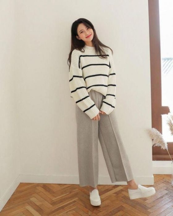 Chica asiática con suéter grande blanco con rayas negras y pantalón gris amplio