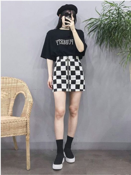 Chica asiática con blusa negra fajada en falda blanca con cuadros negros con calzado negros
