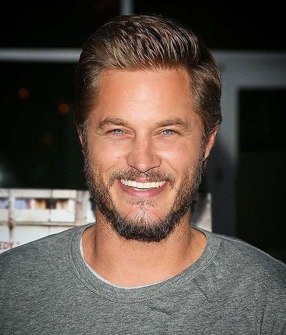 Travis Fimmel sonriendo con suéter gris