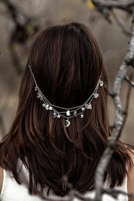 Mujer de espaldas con cabello suelto usando una cadena plateada con detalles de luna y estrellas