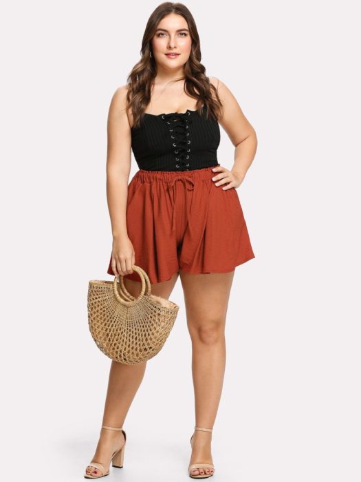 Chica usando outfit veraniego de shorts casuales color ladrillo con top negro, junto con bolsa de paja y tacones