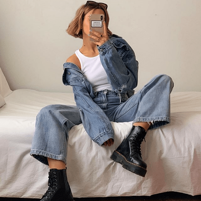 chica usando top blanco sin mangas, chaqueta de mezclilla, pantalones de mezclilla acampanados, botas negras de cuero