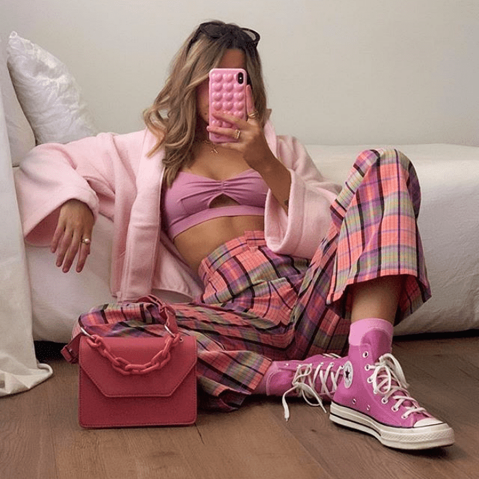 chica usando abrigo rosa, top rosa, pantalones acampanados de cuadros rosas y grises, converse rosas y bolso de mano rosa