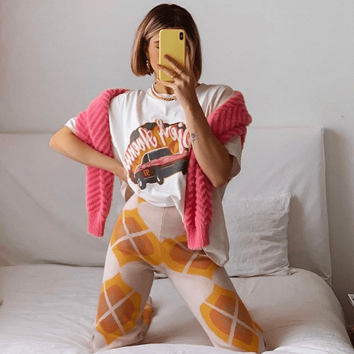 chica usando camiseta blanca con estampado suéter rosa, pantalón color crema con estampado naranja