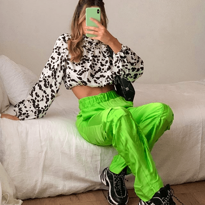 chica usando blusa blanca con negro, pantalones neón verdes y tenis negros