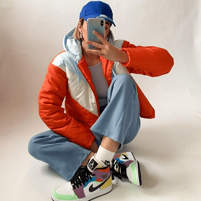 chica usando gorra azul, chamarra anaranjada, pantalones azules y tenis deportivos multicolor