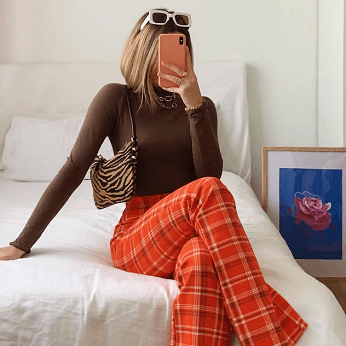 chica usando top café de manga larga, pantalones anaranjados acampanados y bolso de mano pequeño