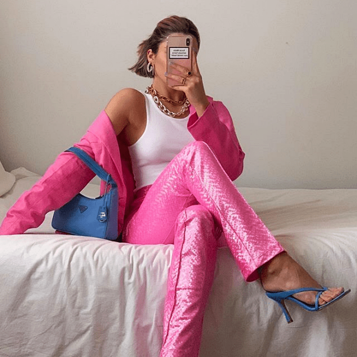 chica usando top blanco sin mangas, chaqueta rosa, pantalón rosa brillante y sandalias de tacón azules con bolso de mano azul