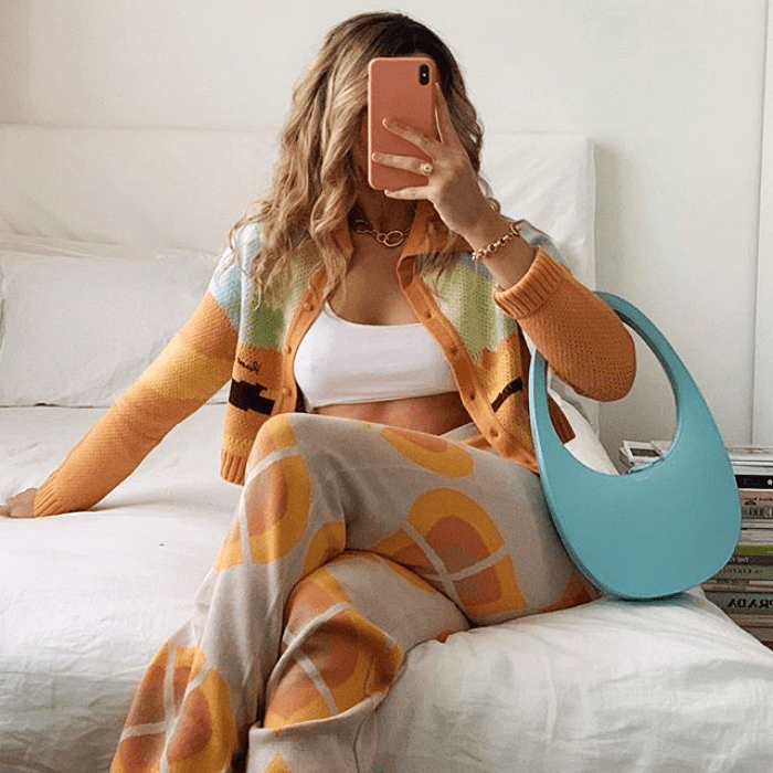 chica rubia usando top blanco, suéter multicolor, pantalón beige con vistas anaranjadas