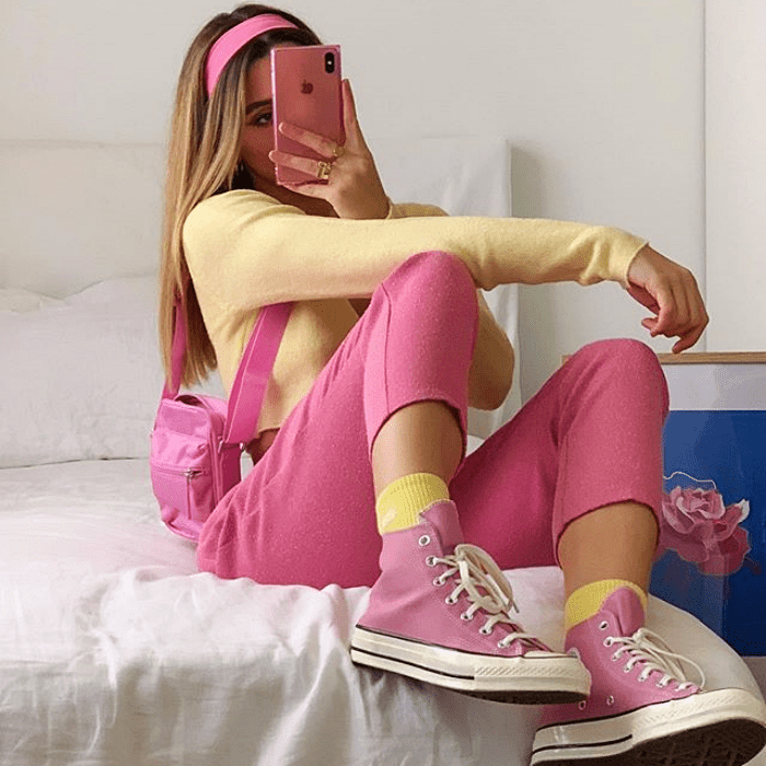 chica usando top de manga larga amarillo, pantalones rosas, calcetas amarillas, converse rosas y bolso de mano pequeño rosa