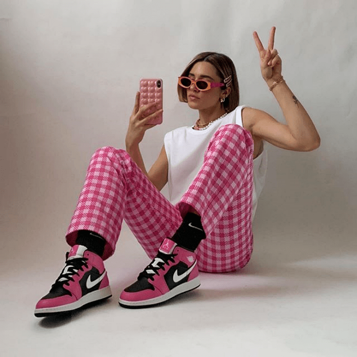 chica usando lentes de sol, top blanco, pantalón rosa de cuadros, tenis deportivos rosas con negro y vistas blancas