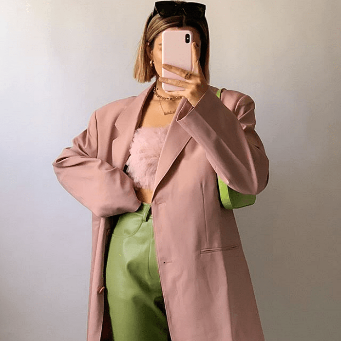 chica de cabello corto usando abrigo de piel rosa, top crop-top rosa, pantalones de cuero verdes y bolso de mano verde