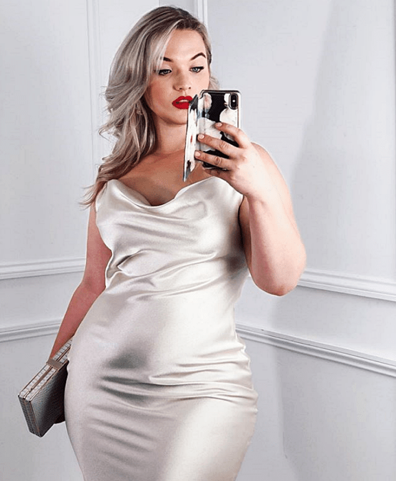 Chica rubia platinada curvy en un vestido gris plateado ceñido con tirantes y escote holgado
