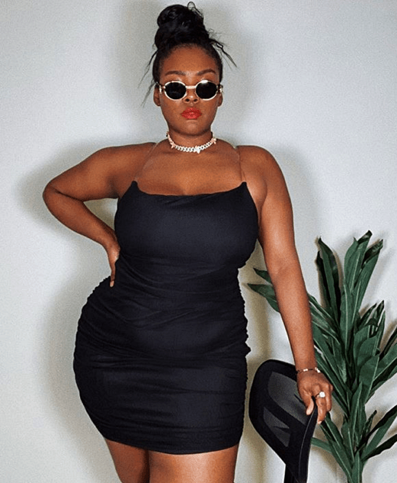Chica morena usando lentes de sol en un vestido negro ceñido con collar