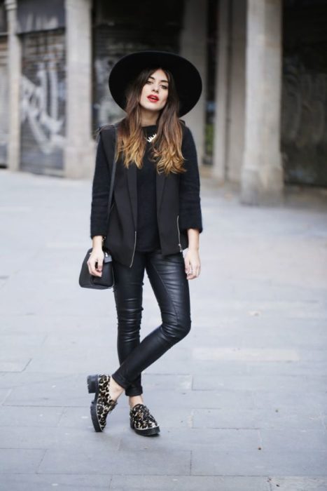 Chica usando un total black look de leggins, blusa y chaqueta de cuero, sombrero y zapatos mocasín con estampado animal print