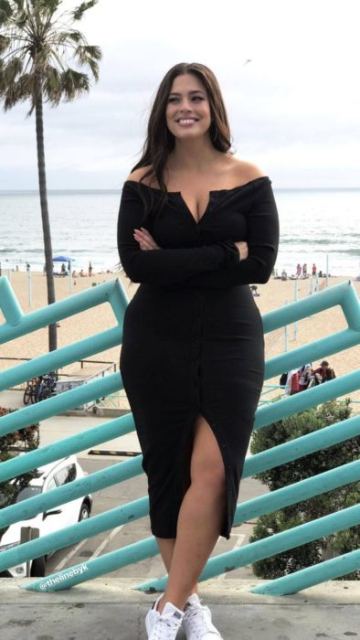Chica usando un total black look de un vestido off the shoulders con abertura en frente y tenis blancos