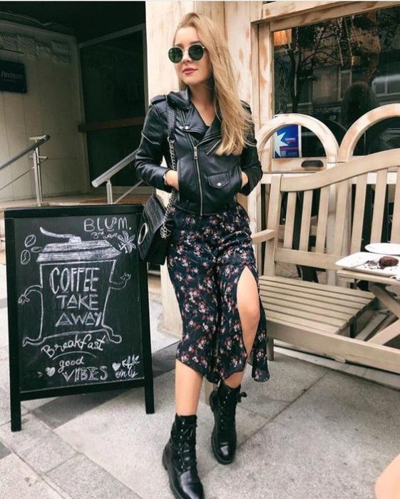 Chica rubia de cabello largo y suelto con gafas de sol oscuras y vestido largo con flores, chaqueta negra de cuero y botas dr. martens