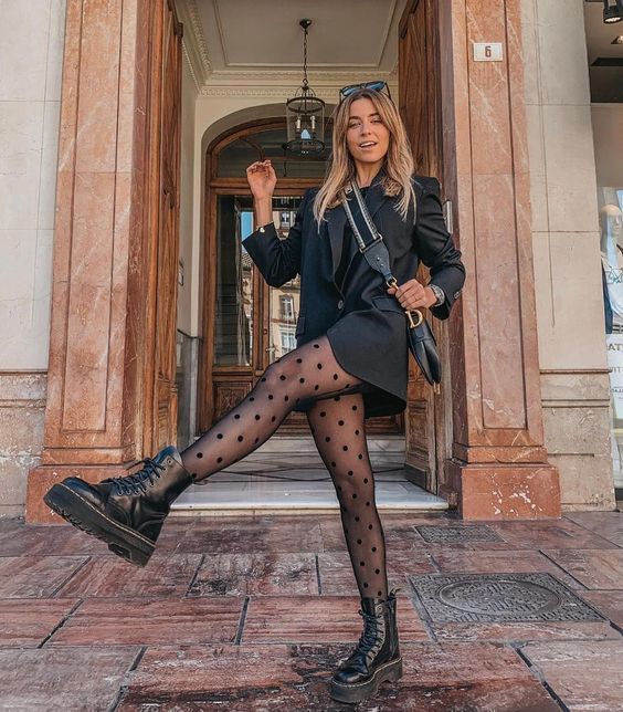 Chica rubia caminando en la calle usando vestido rojo con puntos blancos, chaqueta de cuero negra y botas dr. martens negras