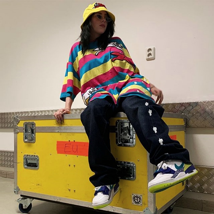 Billie Eilish con un bucket hat amarillo y camisa oversized de rayas