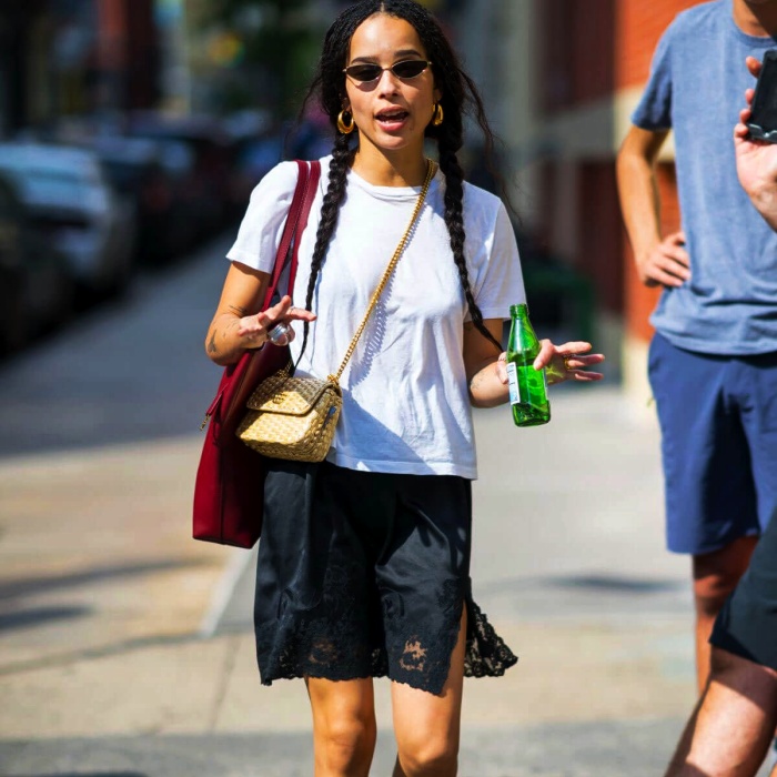 Zoe Kravitz con camiseta blanca, falda azul y bolso de paja