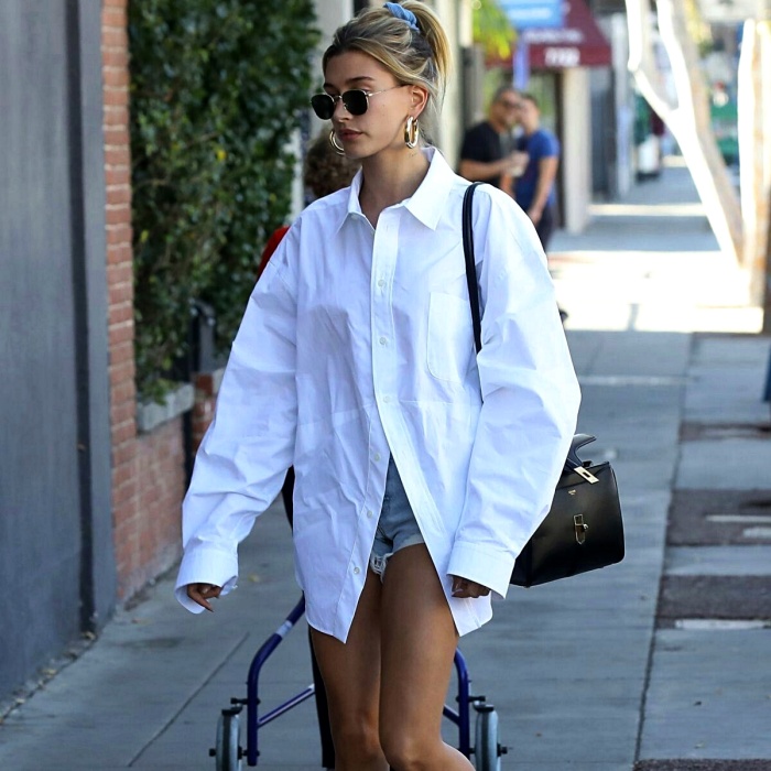 Hailey Bieber con una camisa blanca oversized y shorts de mezclilla
