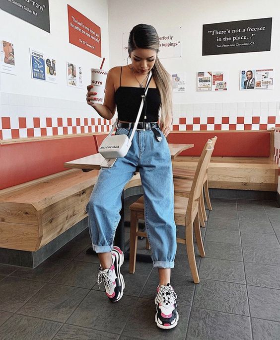 Chica sentada en una mesa con baggy pants de mezclilla y blusa negra de tirantes