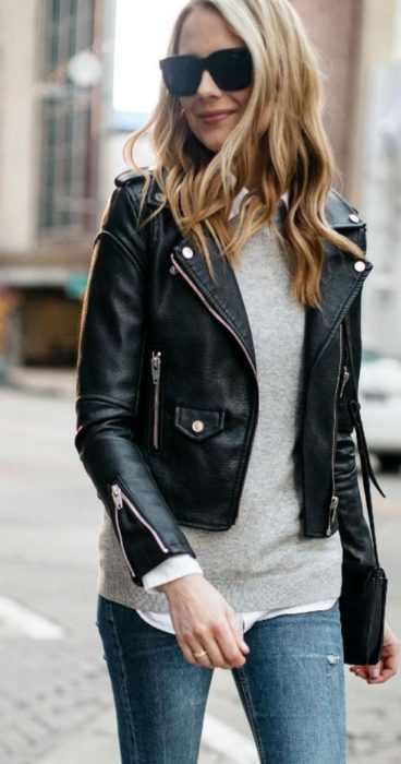 Chica usando suéter crema, jeans, lentes de sol y chamarra biker