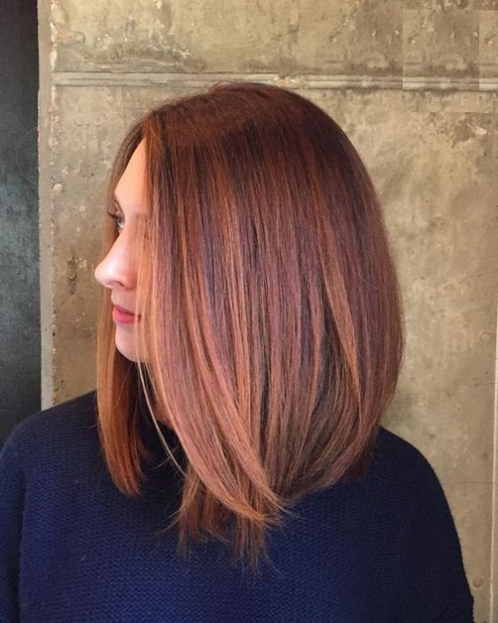 Chica con melena midi mostrando su cabello castaño decorado con mechones peachy copper
