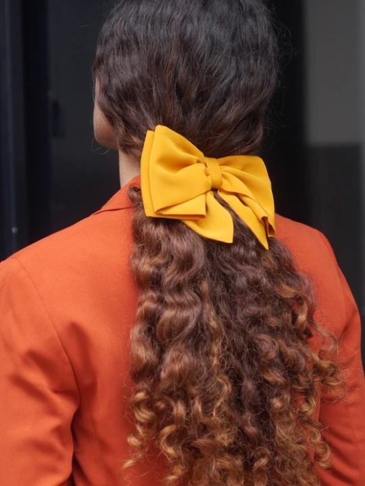 Chica rizada de cabello largo con moño amarillo en una coleta