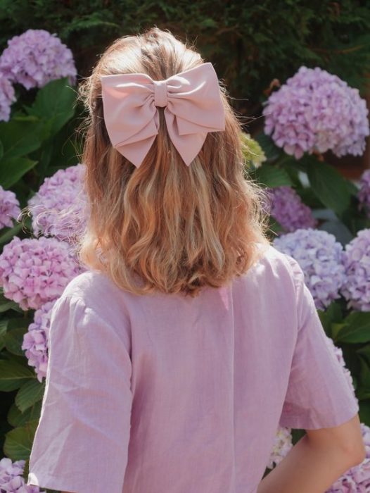 Chica rubia de espaldas con cabello en media cola con moño rosa