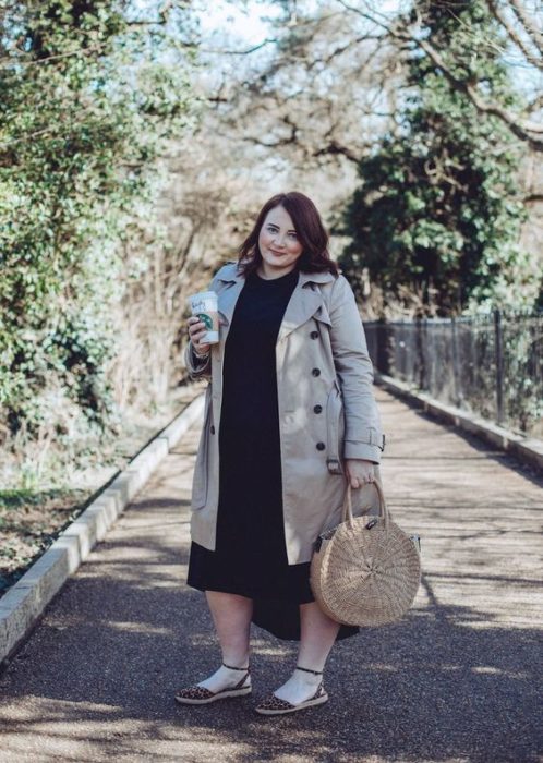 Mujer plus size con gabardina beige y vestido negro, llevando un bolso circular tipo canasta